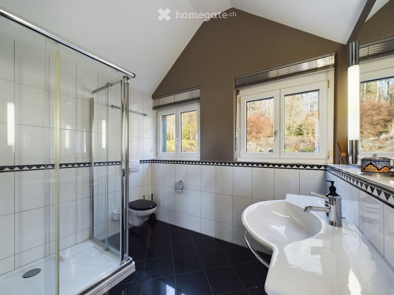 Modern bathroom with white tiles, black accents, a glass-enclosed shower, a toilet, a sink with a modern faucet, and a decorative soap dispenser on the counter.