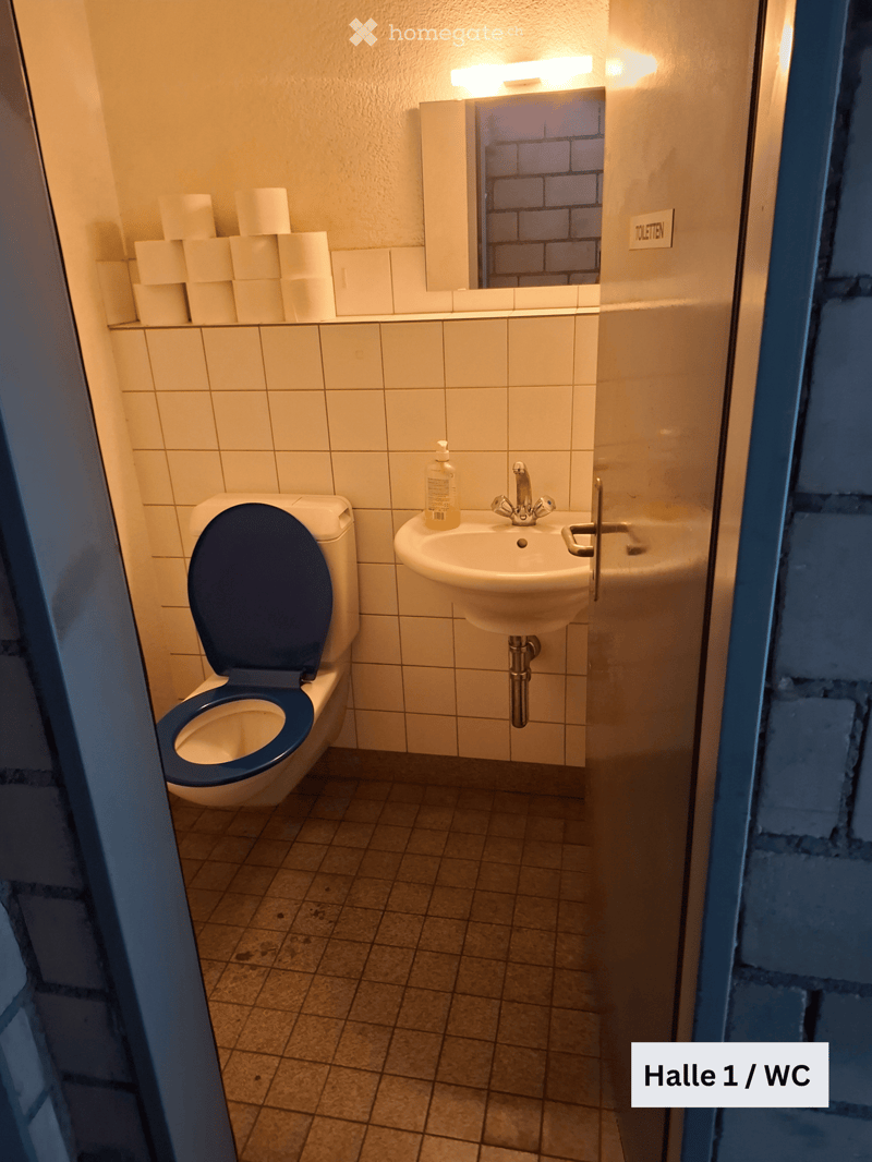 Small bathroom with a toilet, sink, and soap dispenser. The walls are tiled, and there is a mirror above the sink.
