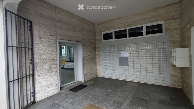 Empty hallway with mailboxes, a door leading to another area, and a small window above the mailboxes.