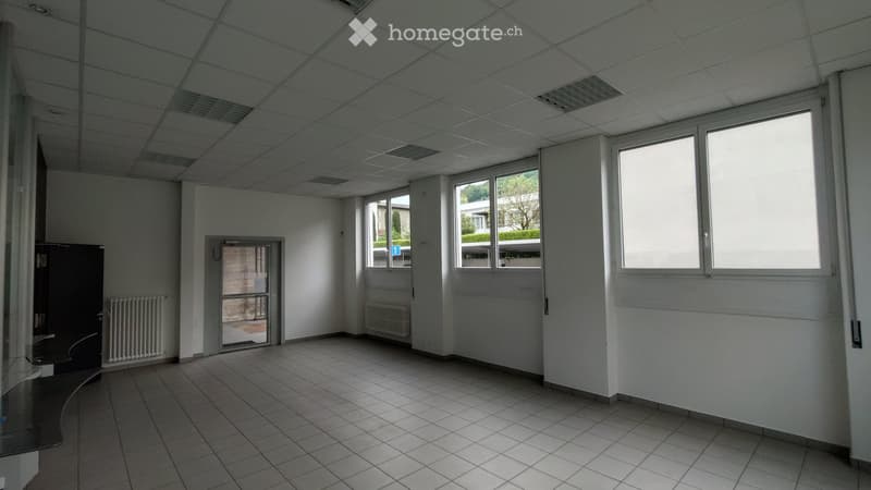 Empty room with white walls, tiled floor, and large windows. No furniture or equipment visible.