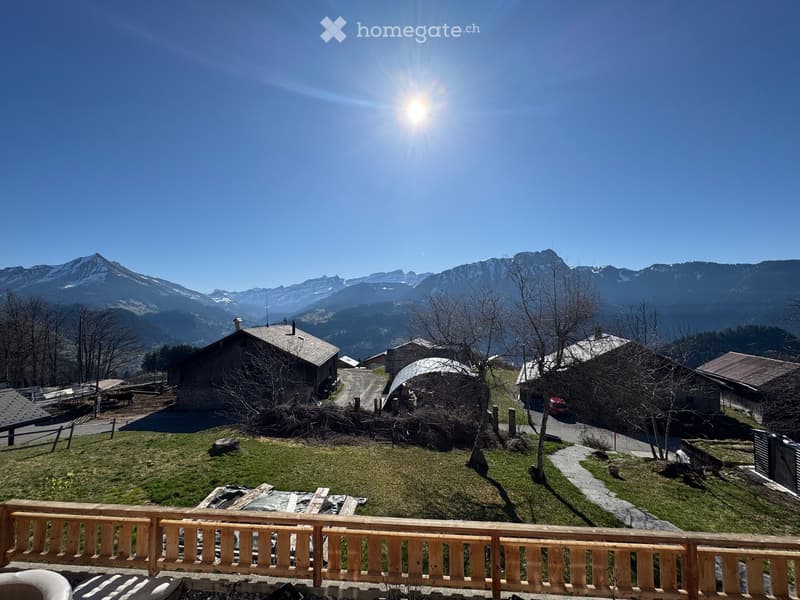 Balcony overlooking a scenic mountain landscape with several houses and a winding road below.