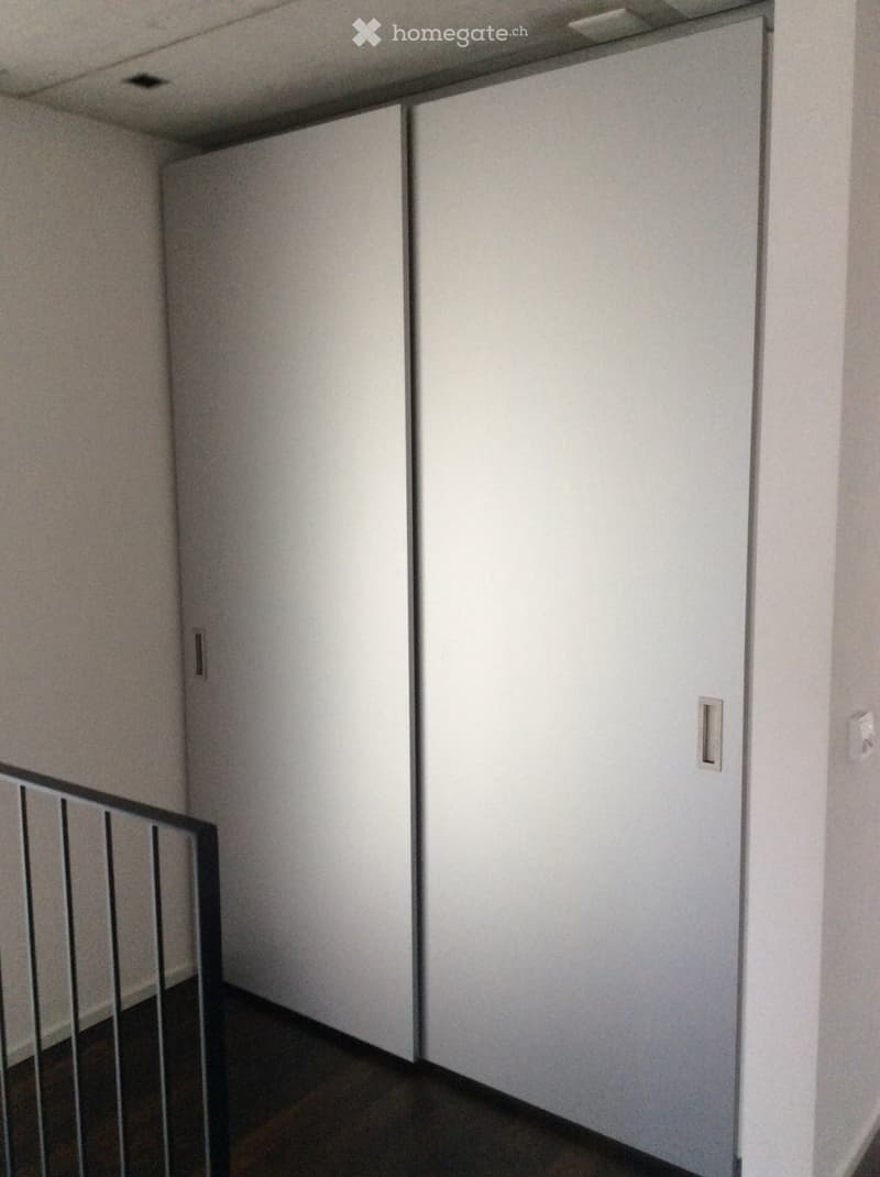 Empty hallway with white walls, dark wooden floor, and closed white doors on both sides.
