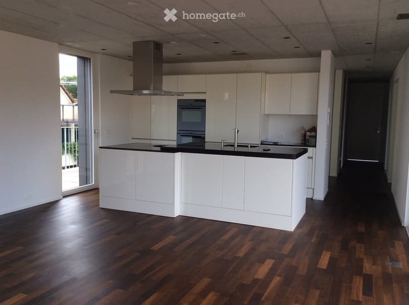 Modern kitchen with white cabinets, a central island, and a dark wooden floor. Features an oven, range hood, and a large window with a view of the balcony.