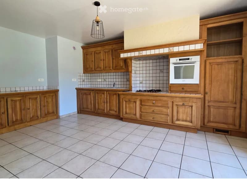 A well-lit kitchen with wooden cabinets, a white oven, a stove, and a sink, featuring tiled walls and a tiled floor.