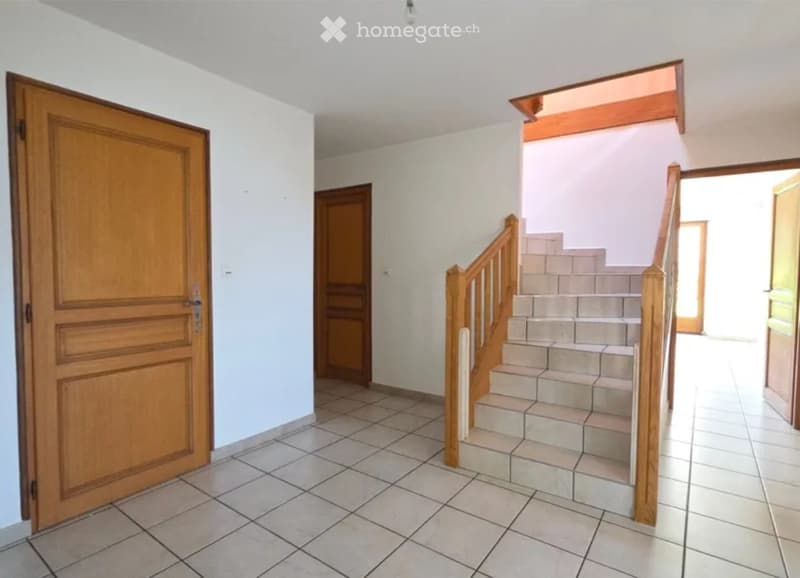 Empty hallway with tiled floor, wooden doors, and a staircase leading upwards.