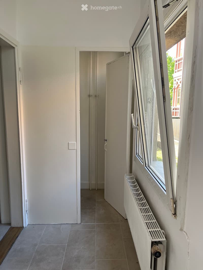 Empty hallway with tiled floor, white walls, radiator, and a door leading to another room.