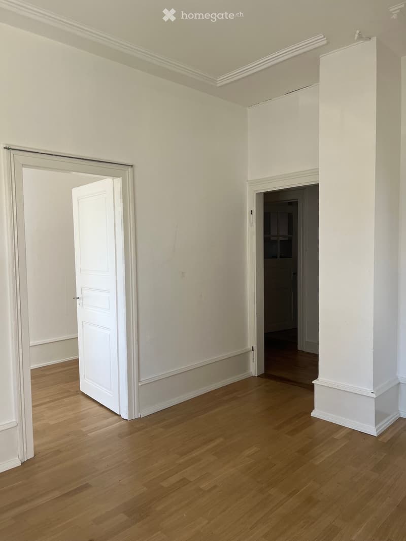Empty room with light wooden flooring, white walls, and two open doors leading to other spaces.