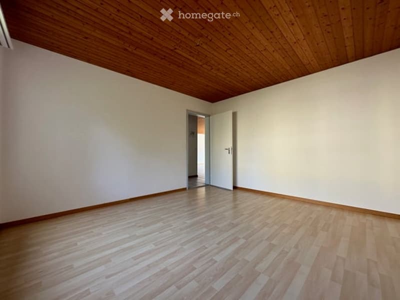 Empty room with wooden flooring and white walls, featuring a wooden ceiling and an open doorway leading to another space.