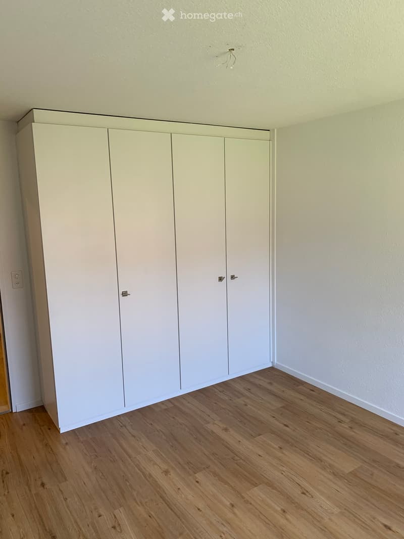 Empty room with light wooden flooring and white built-in closet units against one wall.