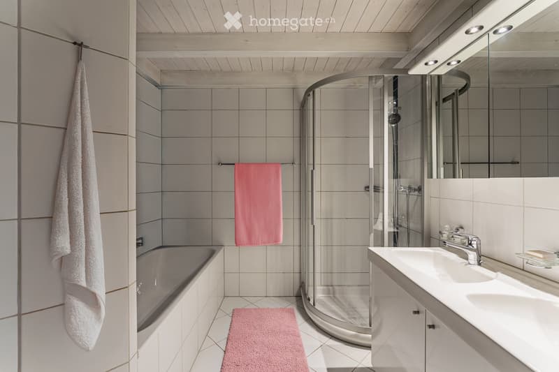Modern bathroom with a bathtub, shower, sink, and mirror. Features tiled walls and a wooden ceiling.