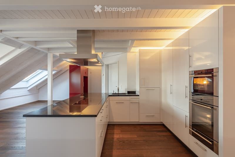 Modern kitchen with white cabinets, dark countertop, stainless steel oven, range hood, and wooden flooring.