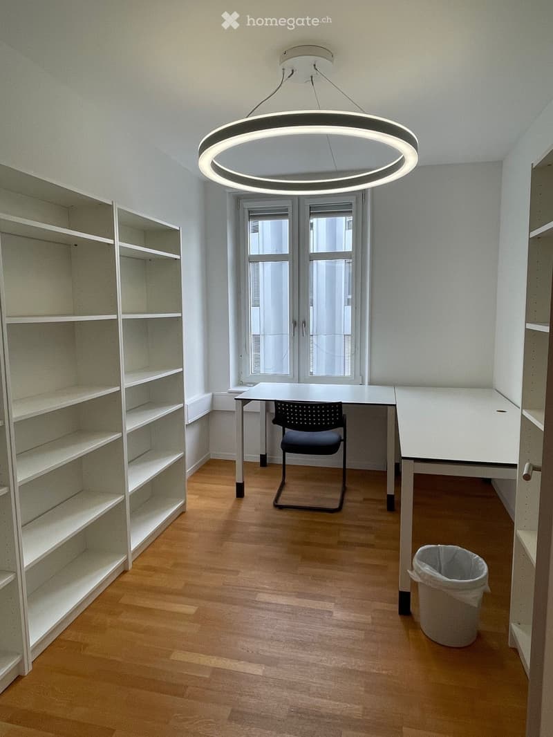 Minimalist room with wooden flooring, white walls, large window, modern round ceiling light, and built-in white shelving units.