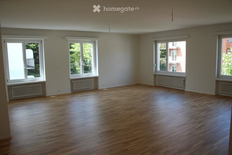 Empty room with wooden flooring, large windows, radiators, and neutral-colored walls.