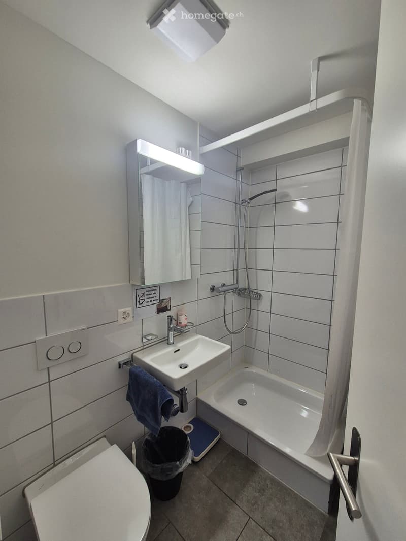 Modern bathroom with white tiles, a sink, bathtub, toilet, mirror, and a towel hanging on the wall.
