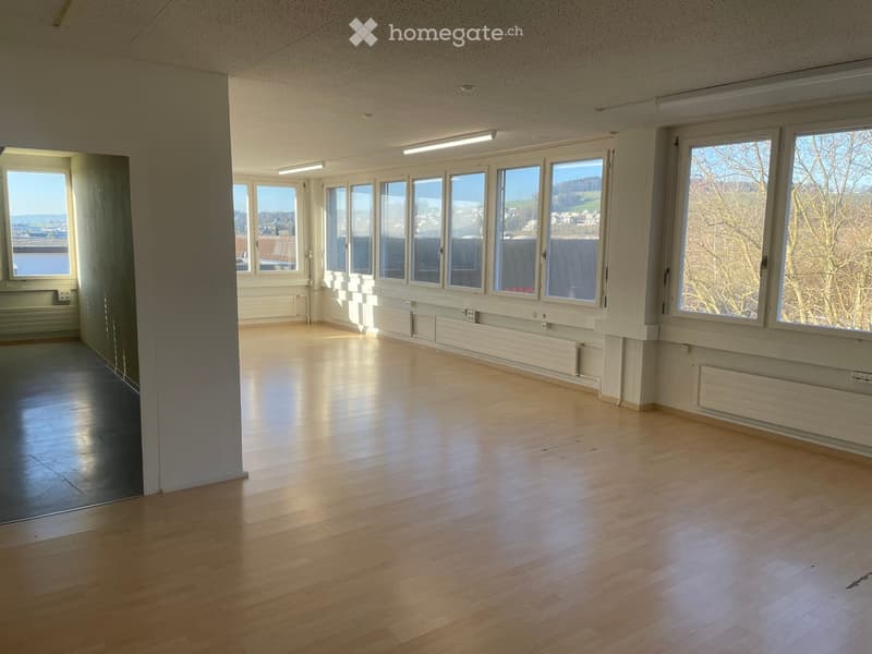 Empty room with wooden floors, windows, white walls, two doors, one with an exit sign