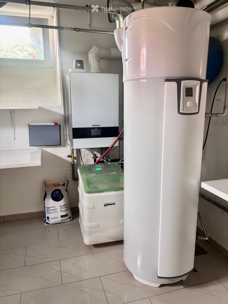 Utility room with a water heater, boiler, control panel, and storage container on the floor.