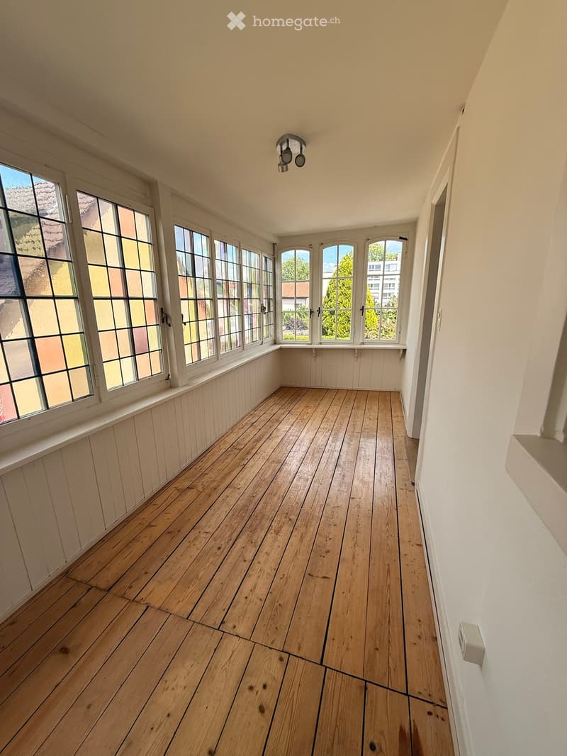 Empty room with wooden flooring, large windows, and white walls.
