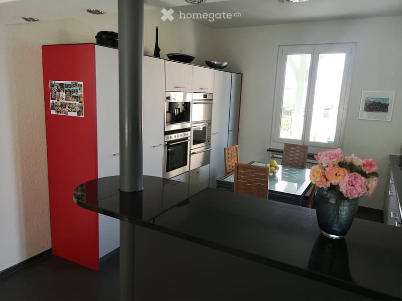 Modern kitchen with white cabinetry, stainless steel appliances, a black countertop, and a dining area with a glass table and wooden chairs.