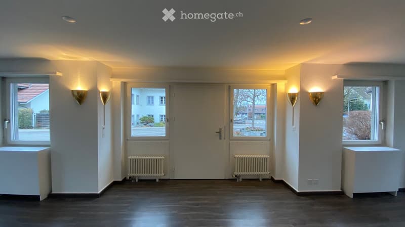 white walls, dark wooden floor, radiators, wall lamps, three windows with balcony