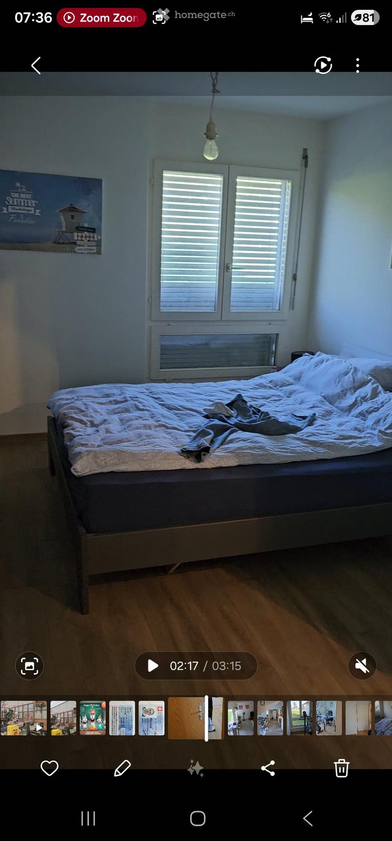 Bedroom with wooden floor, large window with shutters, bed with white bedding, and a poster on the wall.