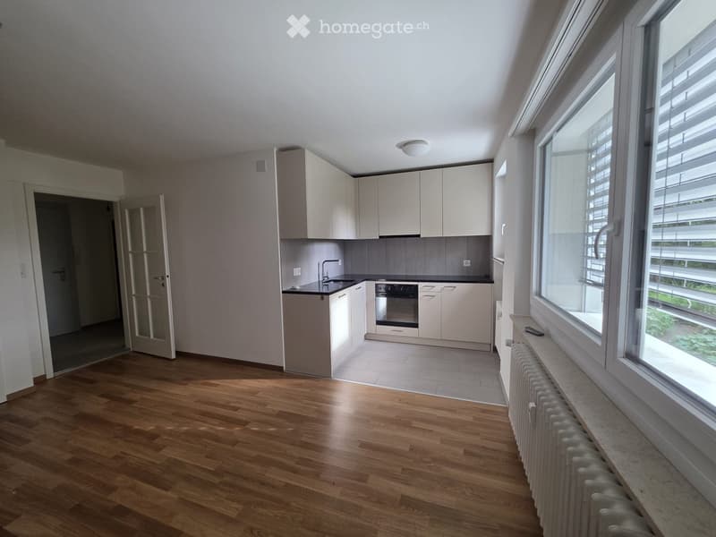 Modern kitchen with light-colored cabinets, a sink, an oven, and a radiator under a large window with blinds.