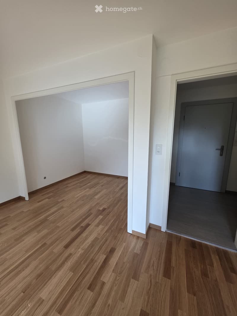 Empty room with light wooden flooring and white walls, featuring two open doorways leading to adjacent spaces.