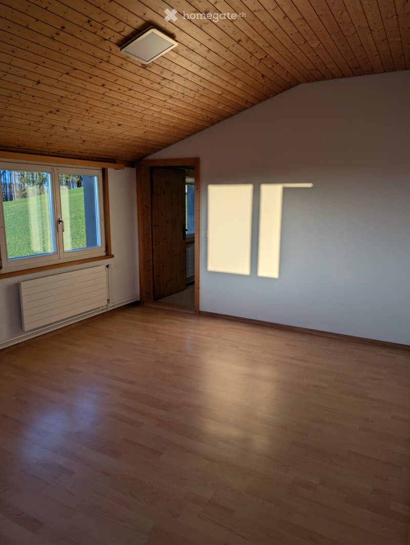 Empty room with wooden floor, white walls, large window, and a door leading to another room. No furniture or equipment present.