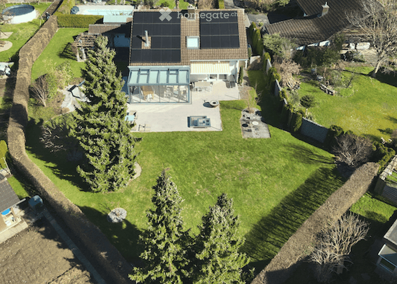 Aerial view of a well-maintained garden with a swimming pool, patio area, and solar panels on the roof of the house.