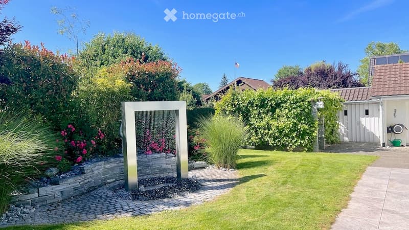 Well-maintained garden with a modern water fountain, lush greenery, and a neatly trimmed lawn.