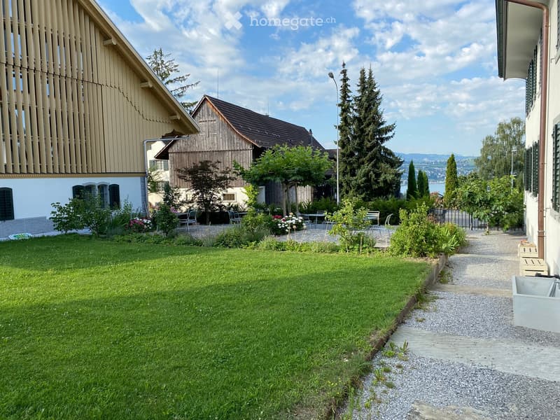 Well-maintained garden with a lawn, gravel pathway, and surrounding buildings with wooden and white facades.