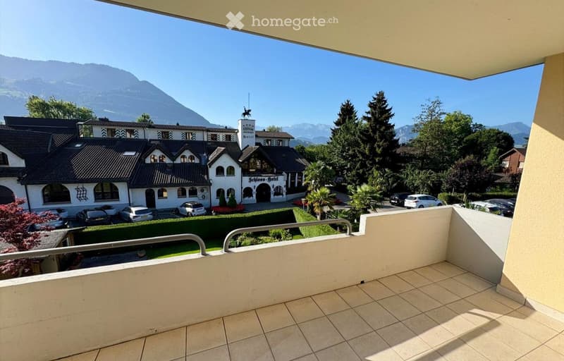 Balcony with tiled floor and metal railing, overlooking a landscaped area with a hotel and mountain view.