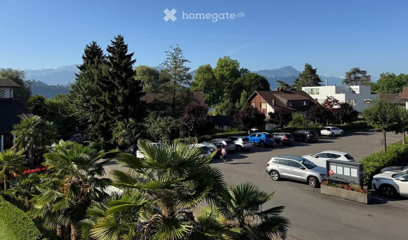 A parking lot surrounded by trees and houses, with a scenic mountain view in the background.