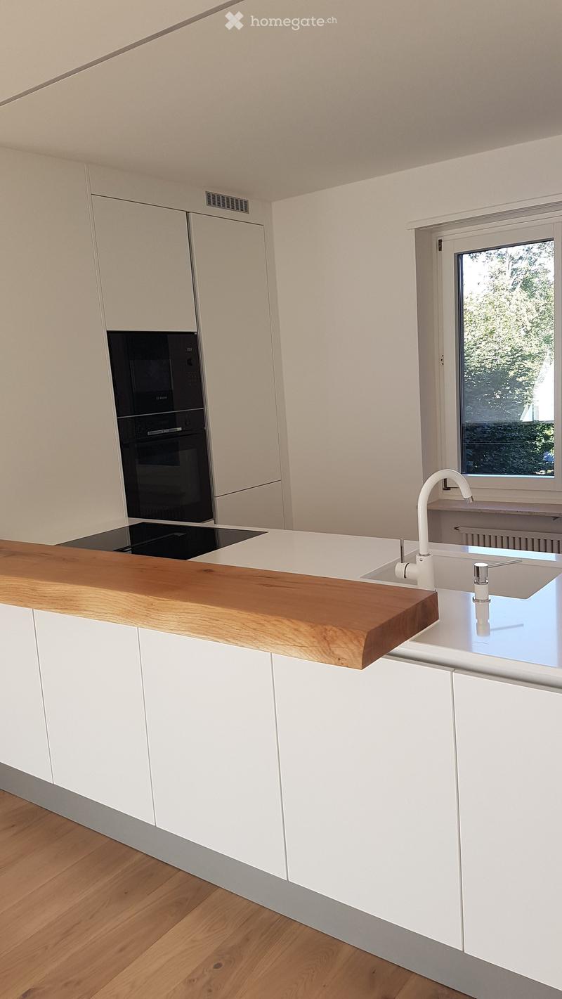 Modern kitchen with white cabinets, wooden countertop, sink, faucet, and built-in oven.