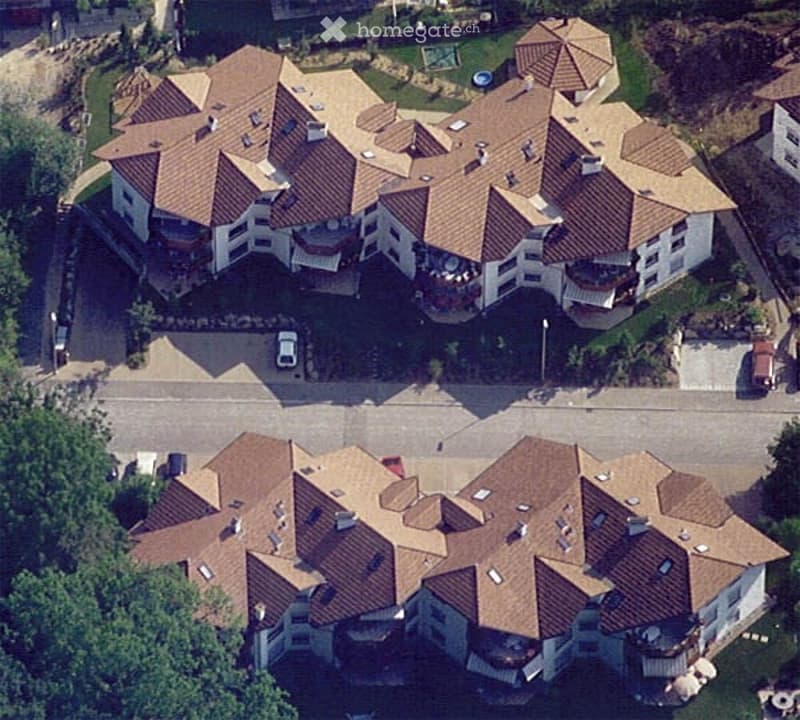 Aerial view of a large residential complex with multiple interconnected buildings, red-tiled roofs, balconies, and surrounding greenery.