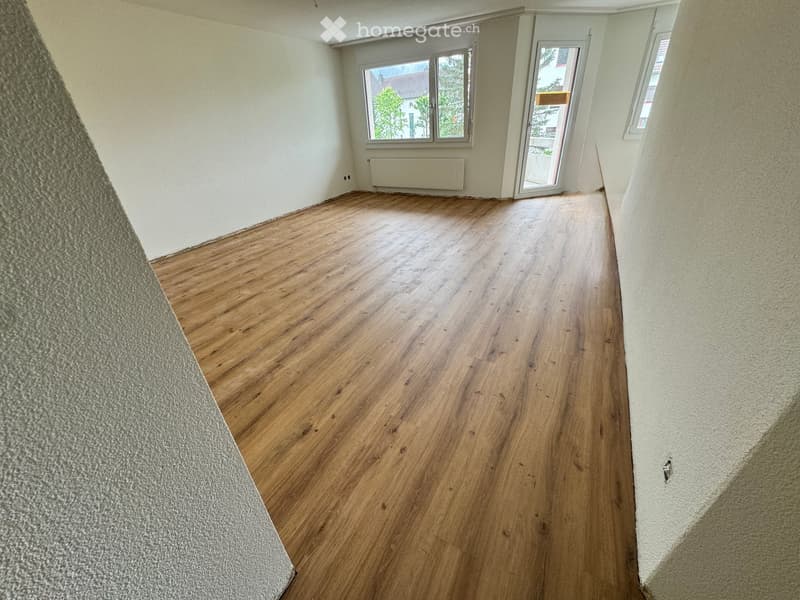 Empty room with wooden flooring, white walls, and large windows with a view of the outside. No furniture or equipment is present.