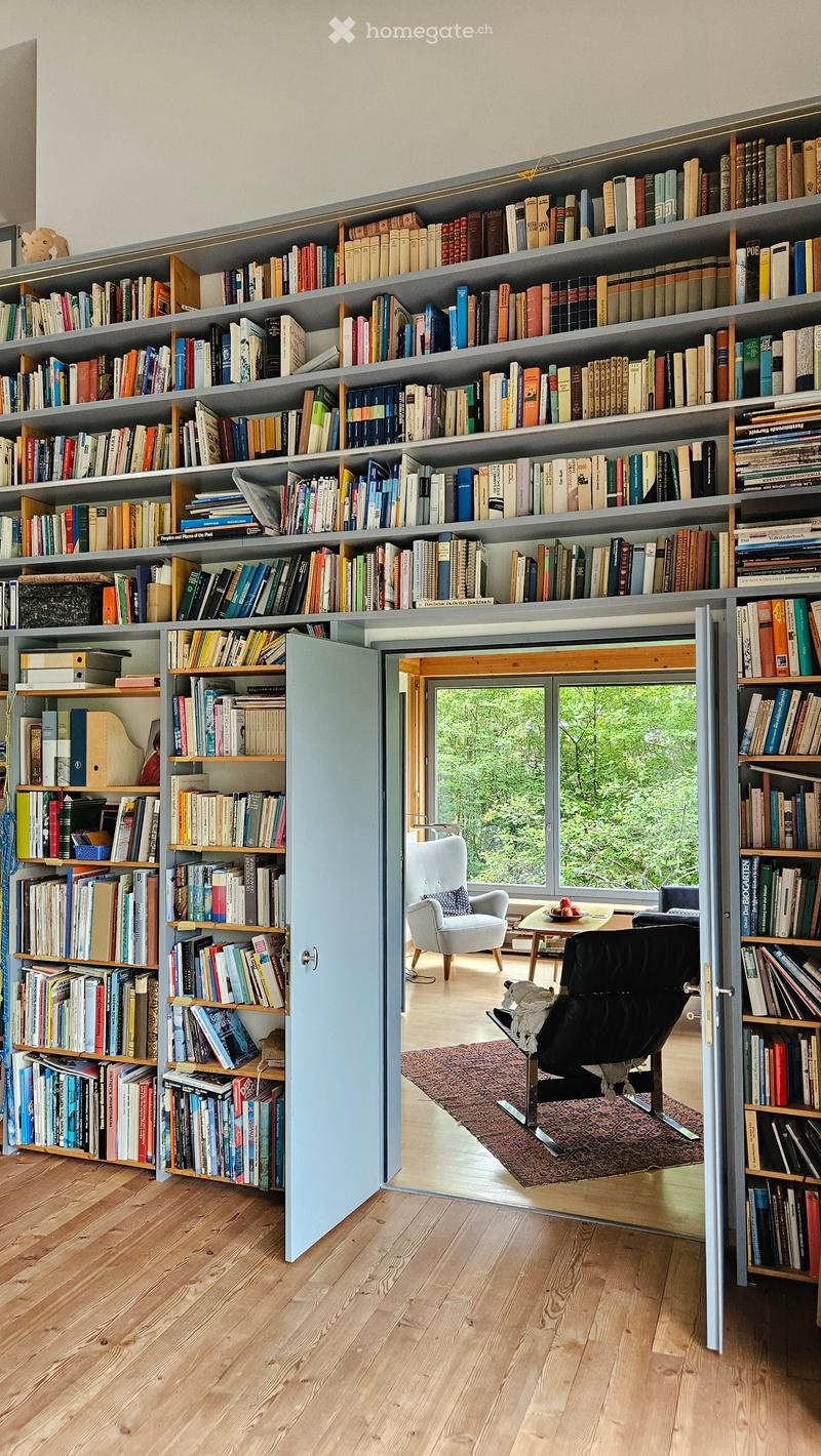 Furnished Room. A room with tall, built-in bookshelves filled with books, a light blue cabinet door, a small seating area with a white armchair, a black leather chair, a small table, and a patterned rug.