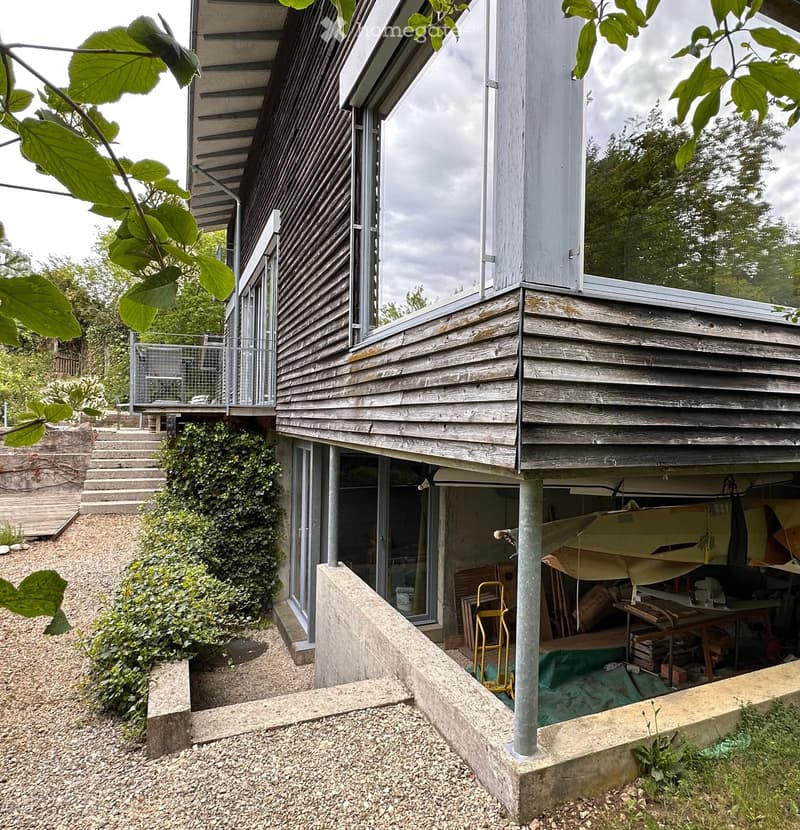 Building. Modern two-story wooden house with large windows, raised ground floor, and a covered garage area.
