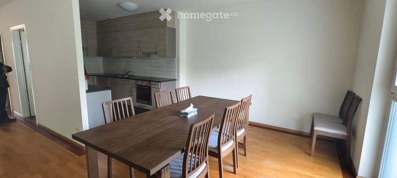 Dining area with a wooden dining table and chairs, a bench with cushions, and an adjacent kitchen area with cabinets, an oven, and a sink.