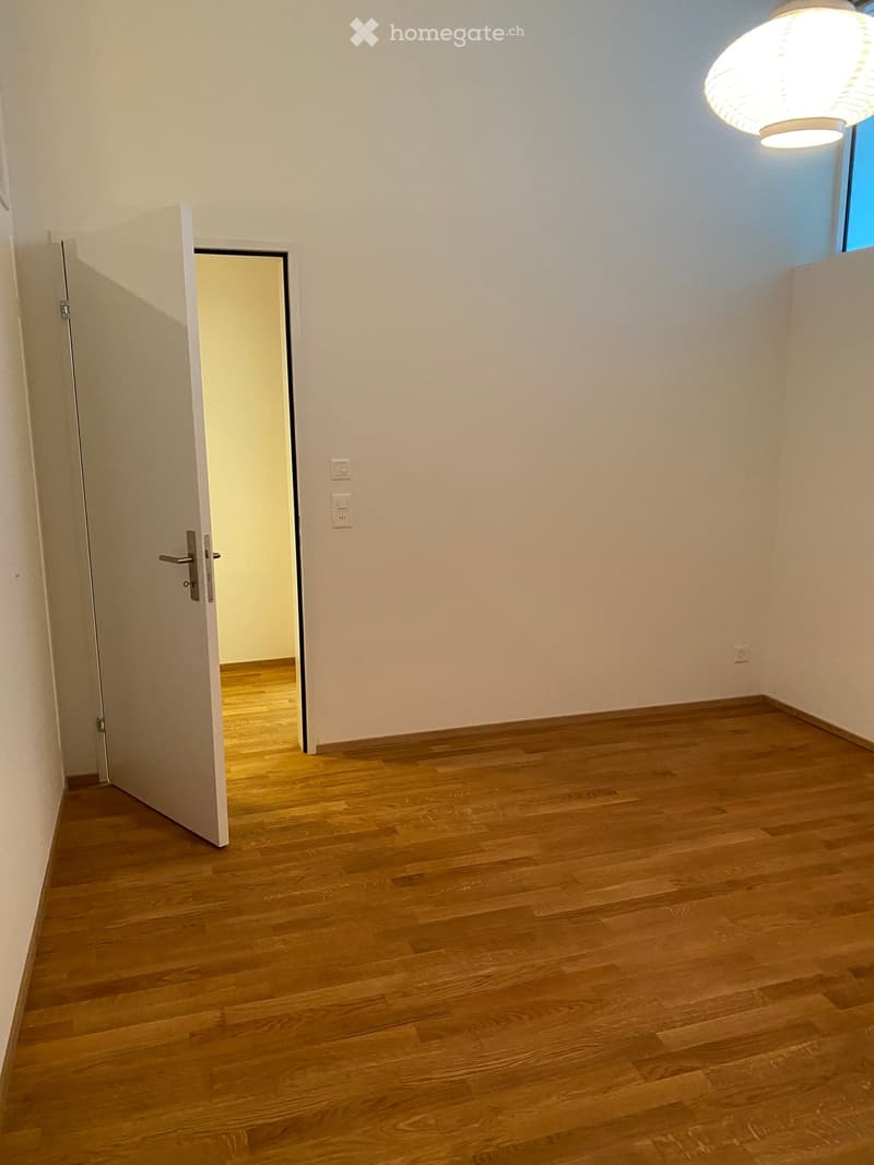 Empty room with wooden floor, white walls, open door, and a small window