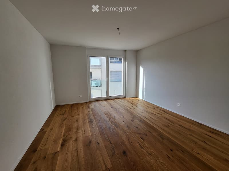 Empty room with wooden flooring, white walls, and large sliding glass doors leading to a balcony.