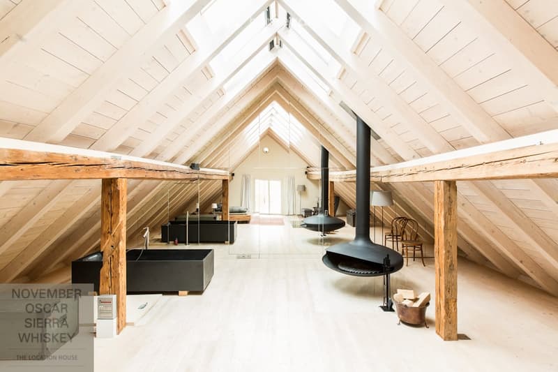 Open loft space with wooden beams, skylights, a fireplace, a sofa, a bathtub, and a chair.