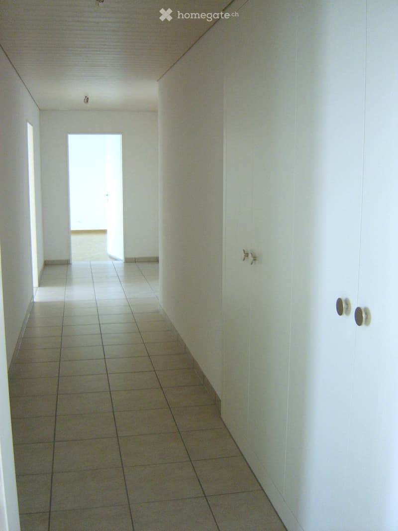 Empty hallway with white walls, tiled floor, and a door at the end leading to another room.