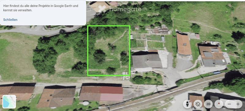 Aerial view of a residential area with multiple buildings, green spaces, and roads. The highlighted area shows a plot of land with a structure partially visible.