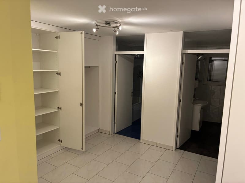 Empty room with tiled floor, white walls, built-in shelving unit, and open doors leading to other rooms.