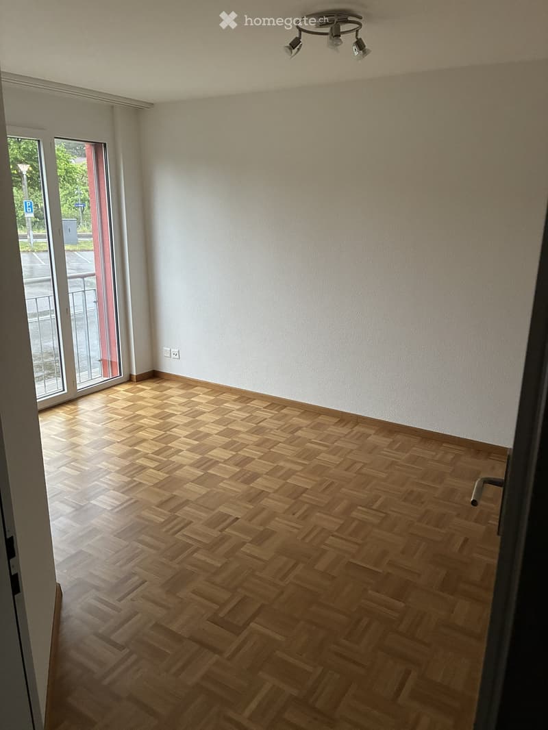 Empty room with wooden herringbone flooring, white walls, and a large sliding glass door leading outside.