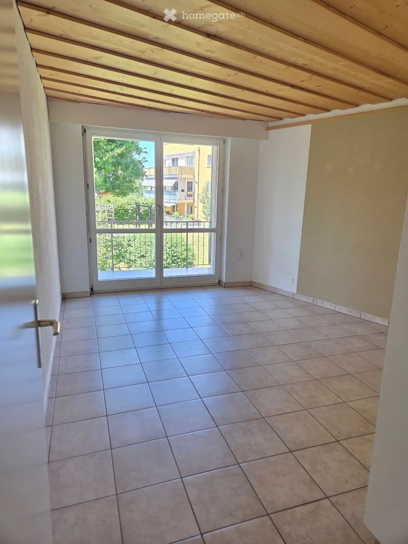 Empty room with tiled floor, white walls, and a sliding glass door leading to a balcony or outdoor area.