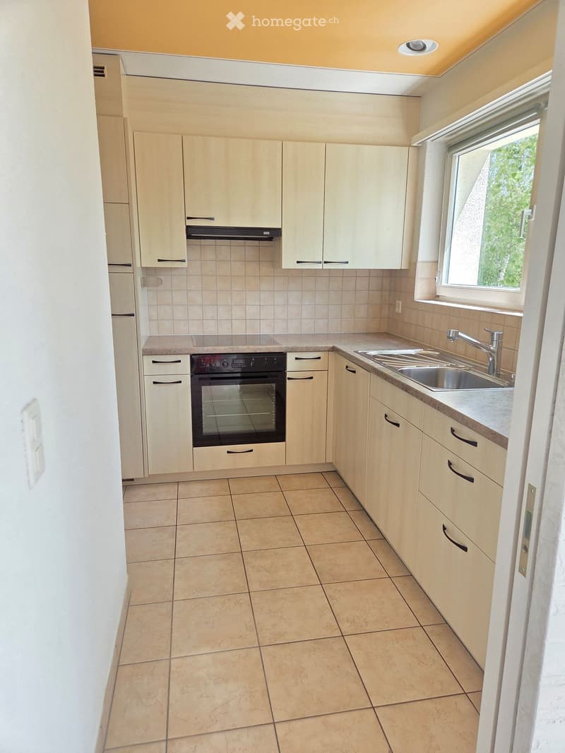 Modern kitchen with light wood cabinets, tiled walls, and a stainless steel sink and oven.