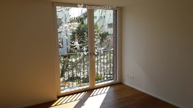 Empty room with wooden flooring, large sliding glass doors leading to a balcony, and white walls.