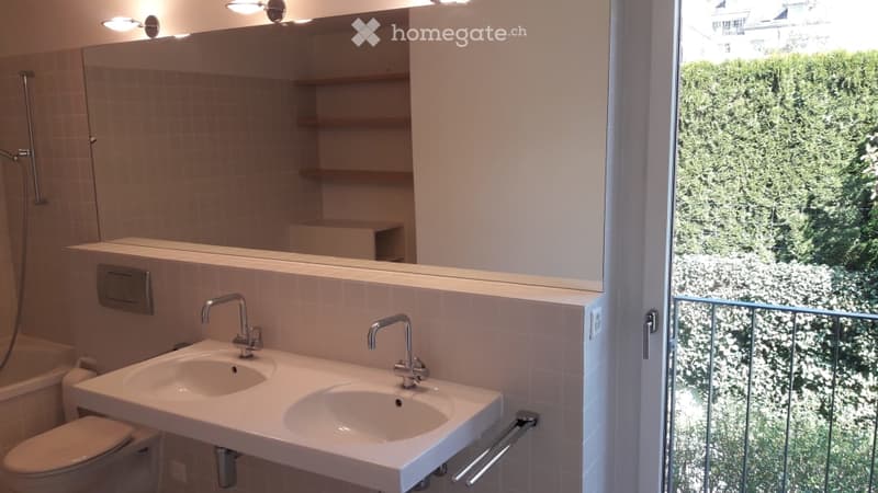Modern bathroom with double sink, large mirror, shelves, and a view of greenery through the window.
