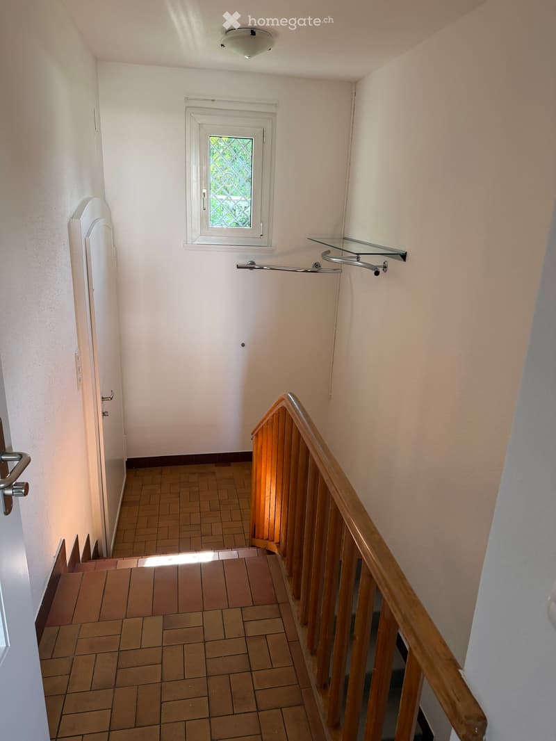 Hallway with tiled floor, wooden staircase railing, glass shelf, and small window with decorative glass.